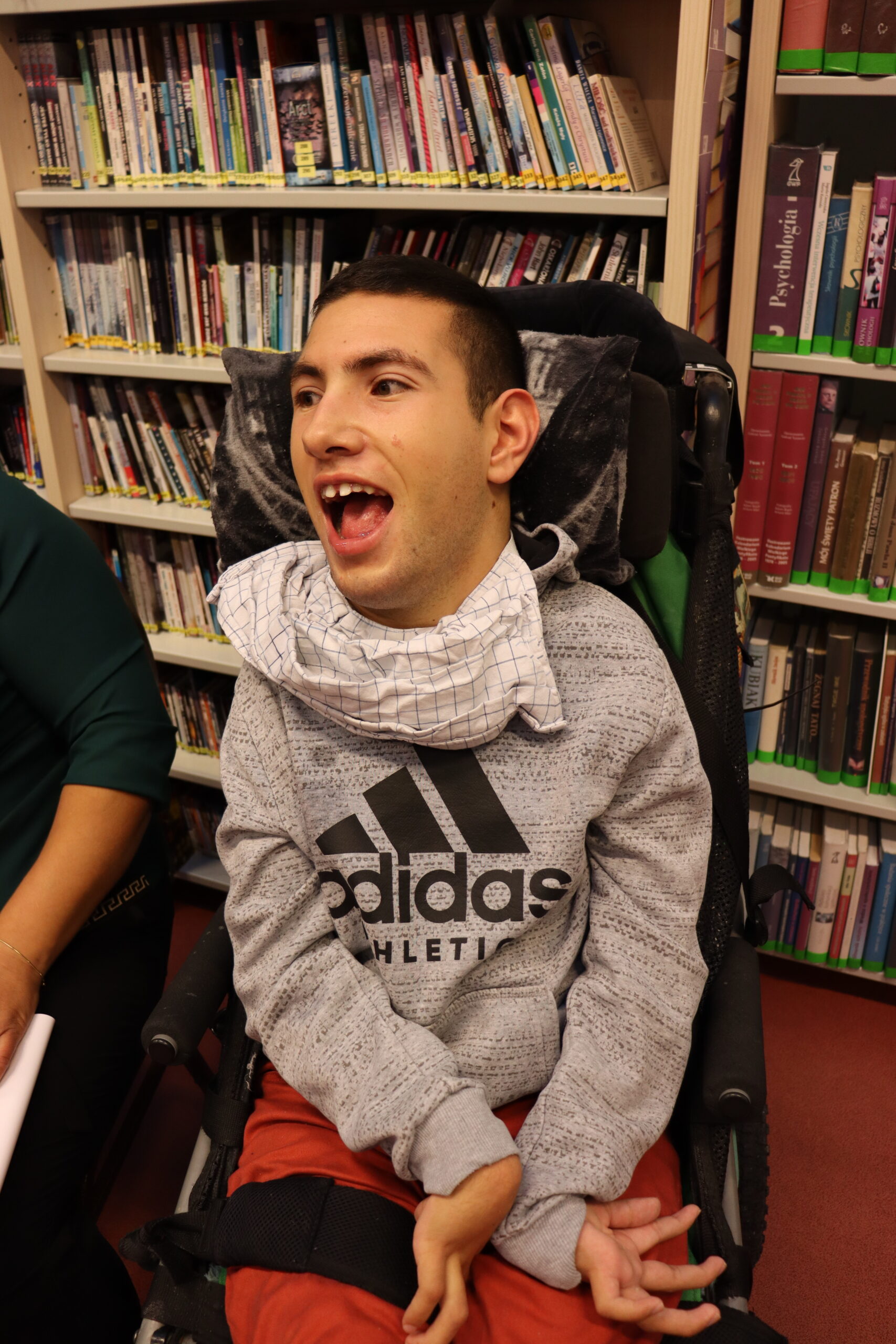 Siedzący na wózku elektrycznym nastolatek pozuje do zdjęcia uśmiechająć się radośnie. 