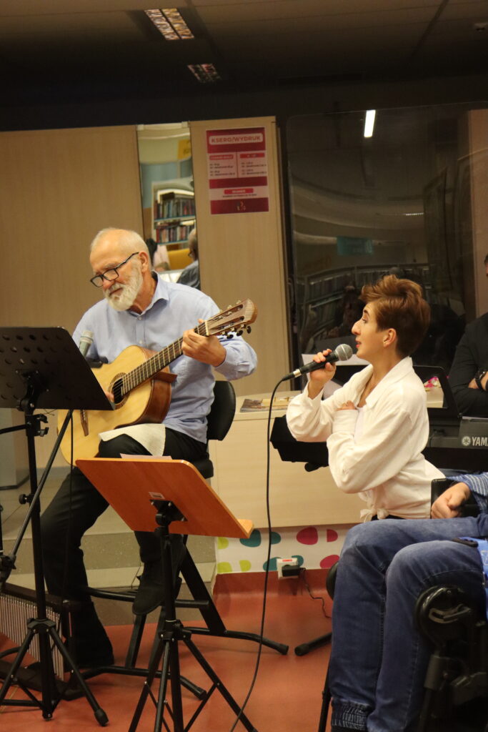 Mężczyzna i kobieta śpiewają. Mężczyzna gra na gitarze.