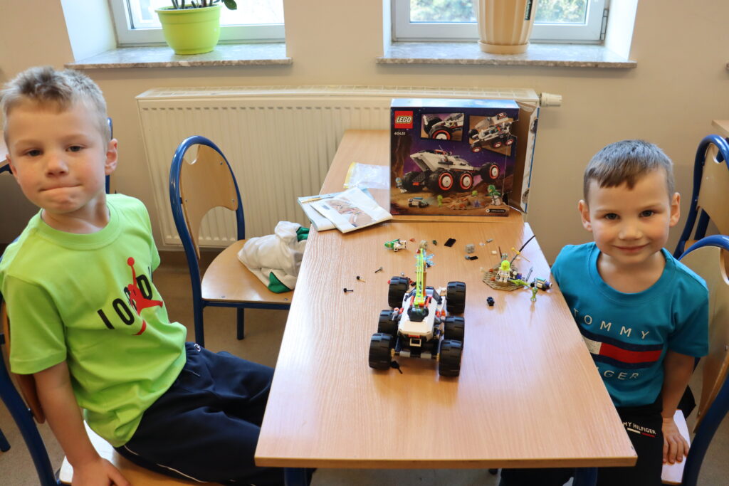 Dwóch chłopców siedzi przy stole, na którym stoi zbudowany przez nich kosmiczny pojazd z klocków lego.