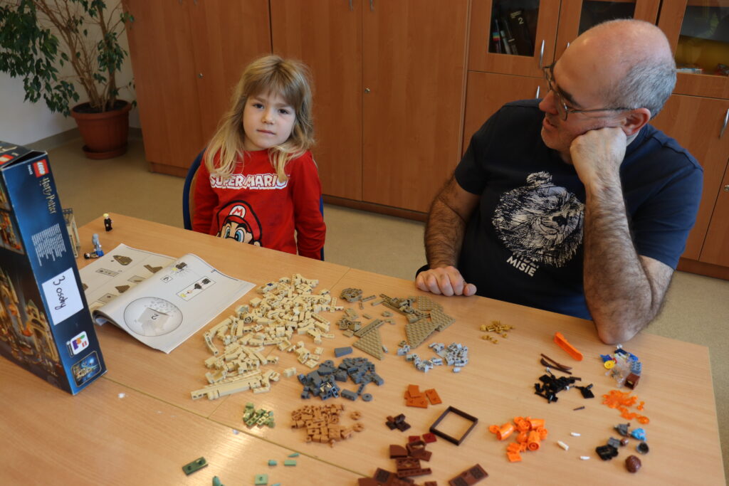 Chłopiec z długimi blond włosami i jego tata siedzą przy stole, na którym leżą posegregowane kolorami klocki z serii Harry Potter.