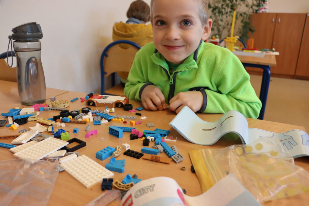 Uśmiechnięty chłopiec w zielonej bluzie buduje z klocków.