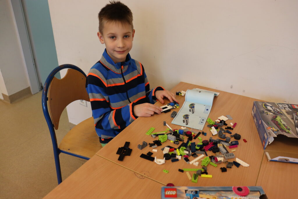 Chłopiec w pasiastej bluzie buduje z klocków lego.