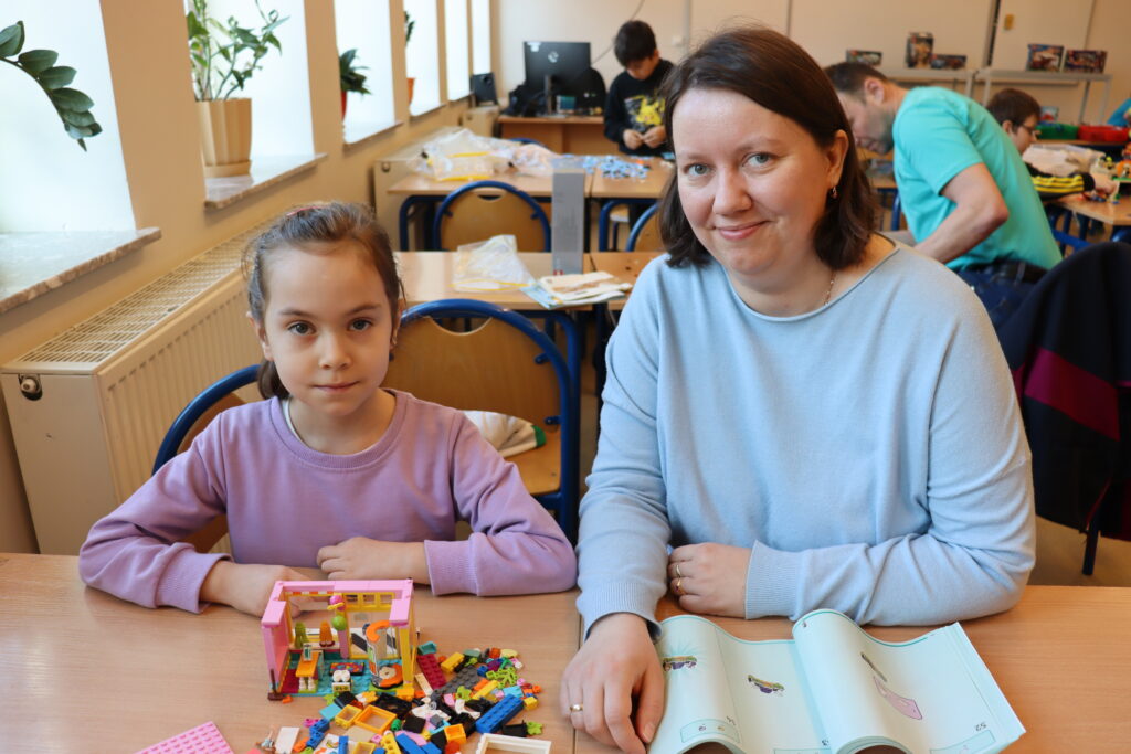 Dziewczynka w różowej bluzie i jej mama budują domek z klocków.