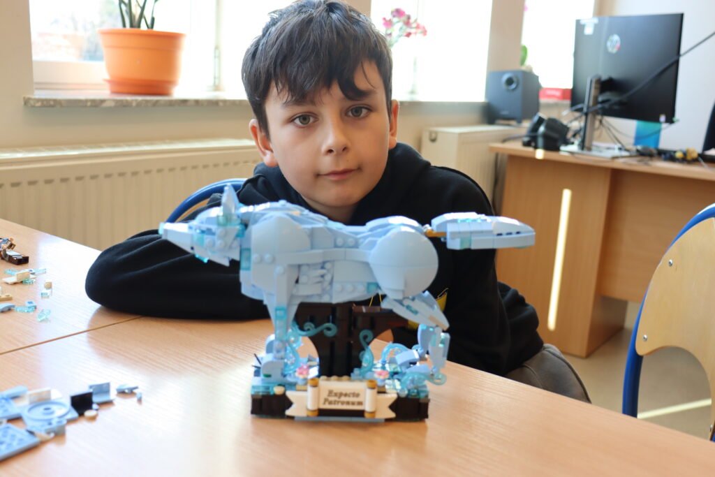 Chłopiec w czarnej bluzie pokazuje zbudowany przez niego zestaw lego: niebieskiego wilka z serii Harry Potter.