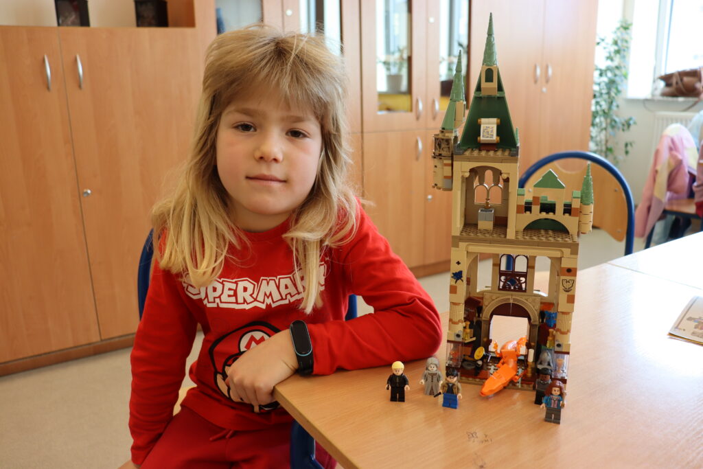 Chłopiec z długimi blond włosami pokazuje zbudowany przez niego zestaw lego: wieżę z serii Harry Potter.