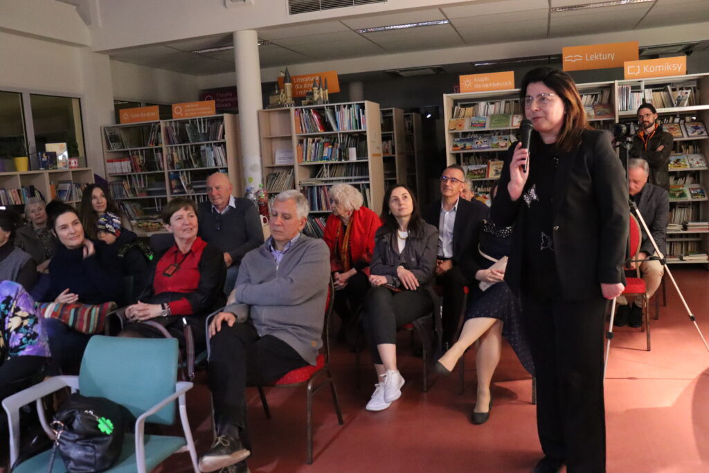 Kobieta w ciemnym eleganckim ubraniu przemawia do mikrofonu.