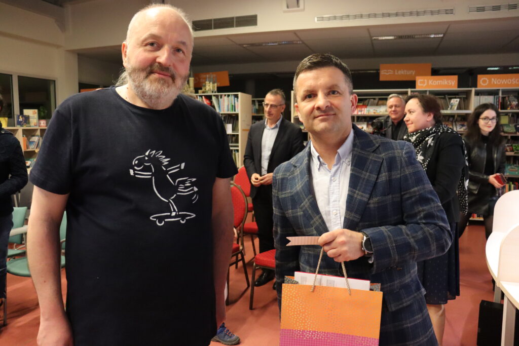 Dwóch mężczyzn pozuje do zdjęcia: po lewej wokalista zespołu, po prawej dyrektor biblioteki.