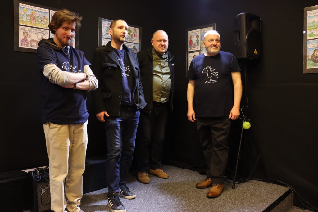 Czterech członków zespołu pozuje do zdjęcia na scenie.