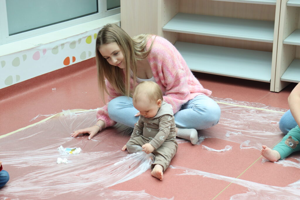 Zbliżenie na dłonie dziecka bawiącego się miękkimi, niebieskimi piórami w plastikowym pudełku.