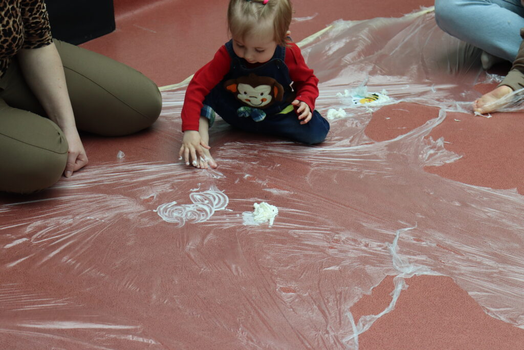 Dziecko na folii bawi się śmietanką bitą.