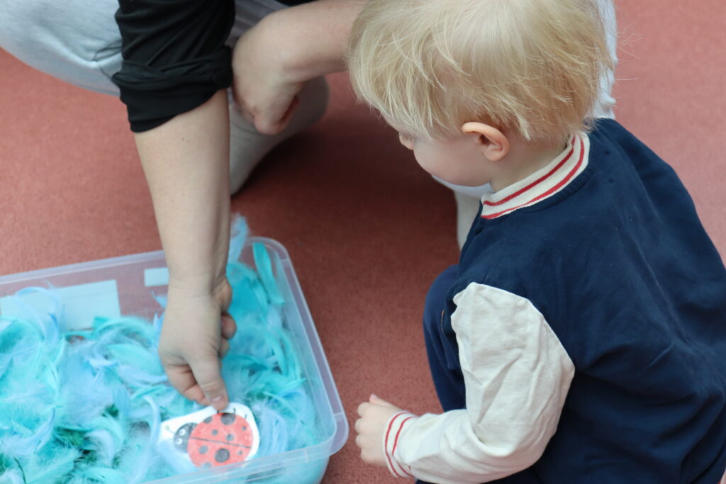 Kobieta pochyla się nad dzieckiem, które bawi się piórami;