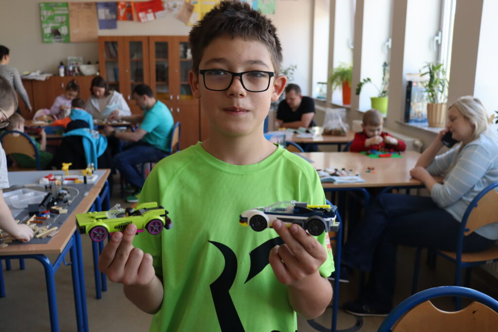 Chłopiec w zielonej koszulce pokazuje zbudowane przez siebie samochody.