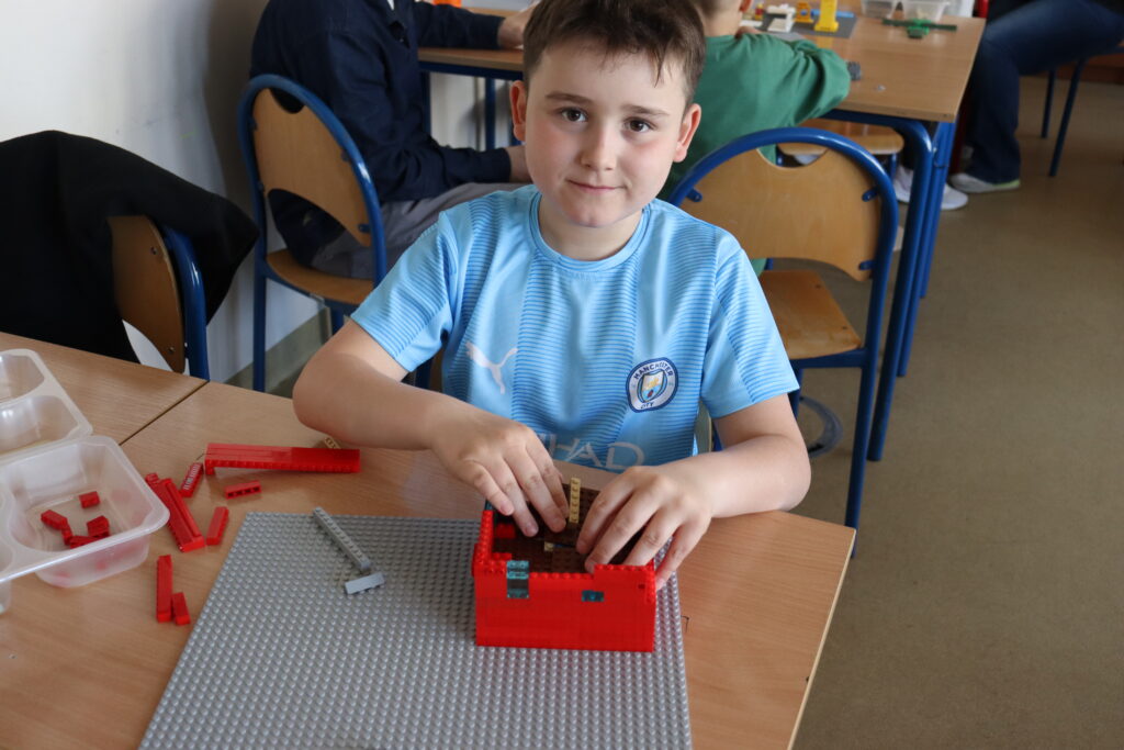 Chłopiec w niebieskiej koszulce buduje domek.