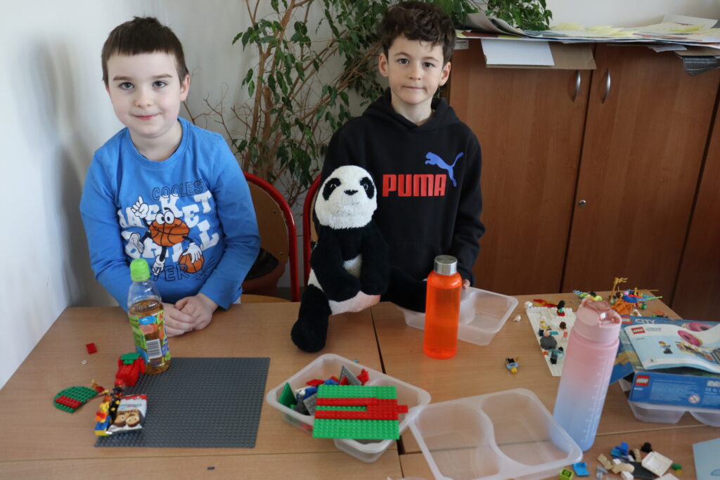 Dwóch chłopców stoi przy stole, jeden trzyma pluszową pandę.