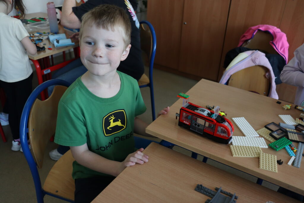 Maly chłopiec siedzi przy tramwaju z klocków lego.