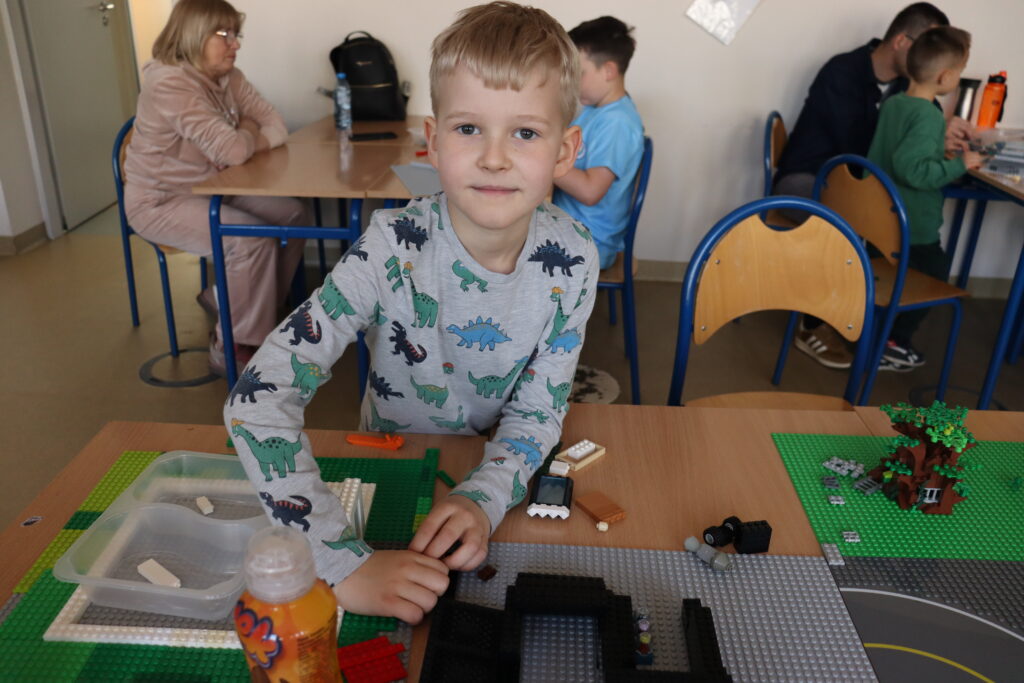 Chłopiec w koszulce w dinozaury buduje z klocków.