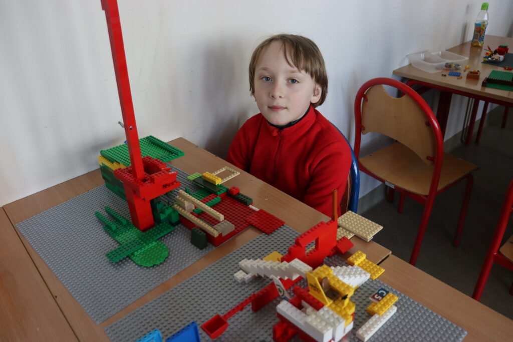 Chłopiec w czerwonej bluzie siedzi przy zbudowanej przez siebie wieży.