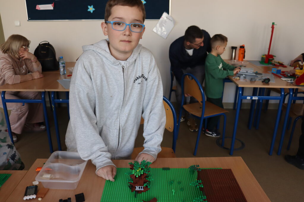 Chłopiec w okularach pokazuje zbudowane przez siebie drzewo.