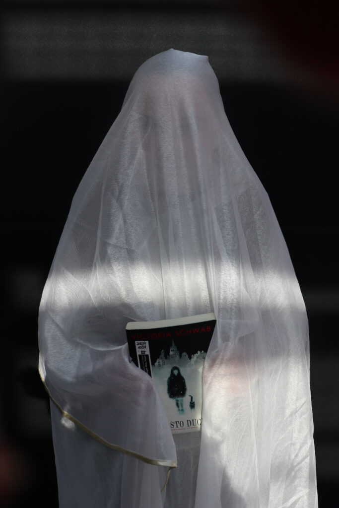 Dziewczynka w przebraniu ducha, przykryta tiulową firanką, trzyma książkę "Miasto duchów".