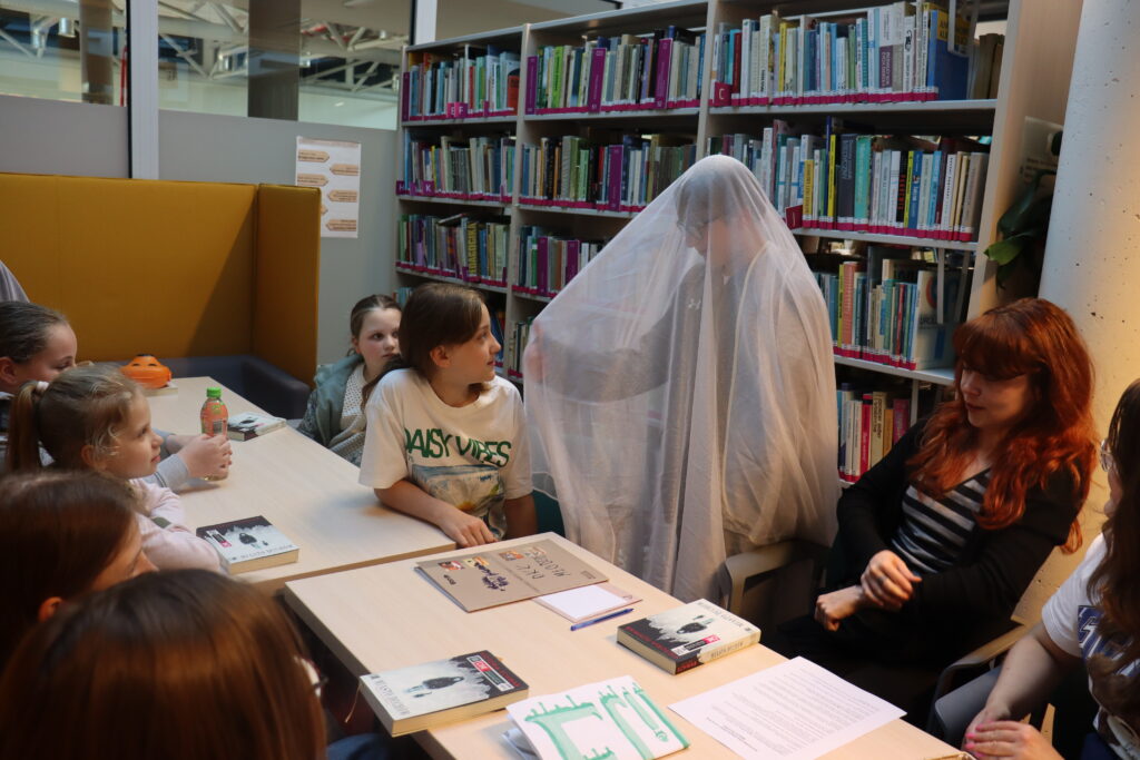 Chłopiec w przebraniu ducha, przykryty tiulową firanką, rozmawia z dziewczynką w jasnej koszulce.