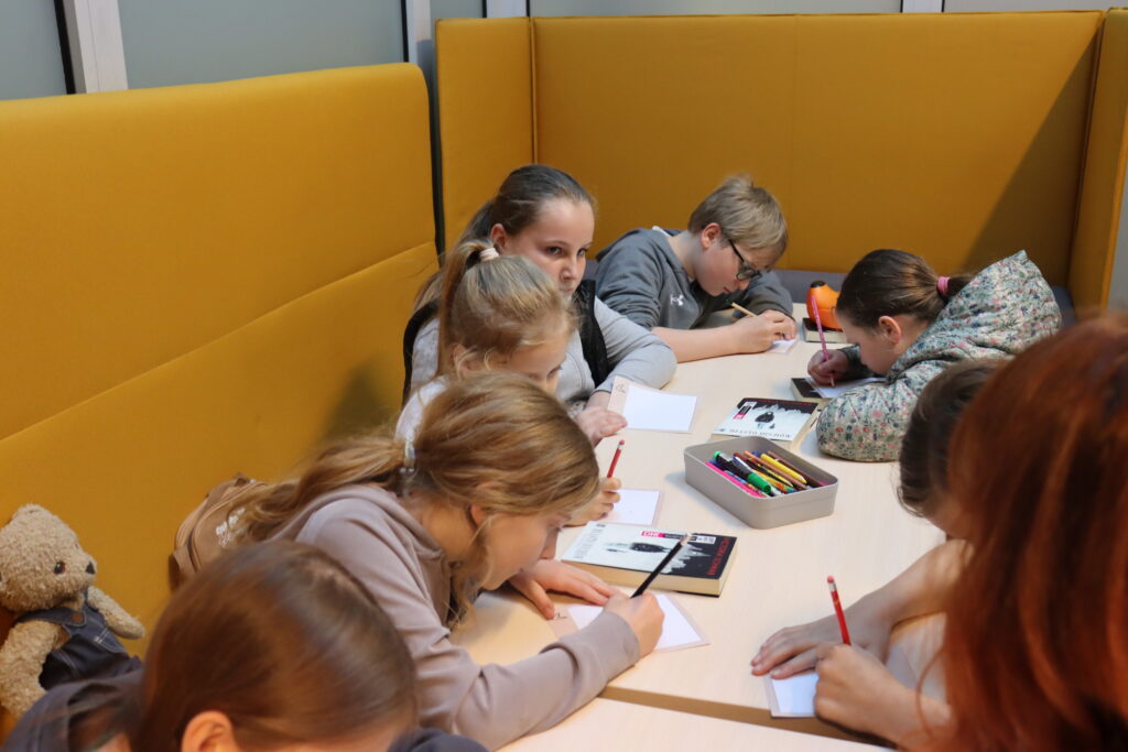 Grupa dzieci przy stole rysuje na kartkach.