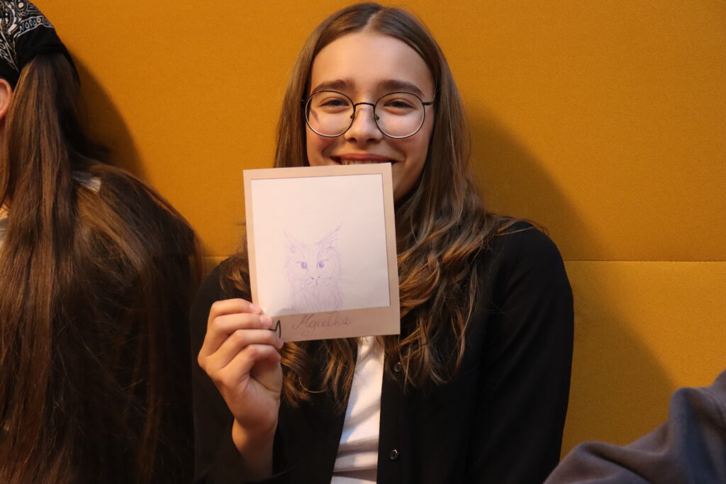 Dziewczynka w okularach prezentuje swój rysunek: kot mgiełka.