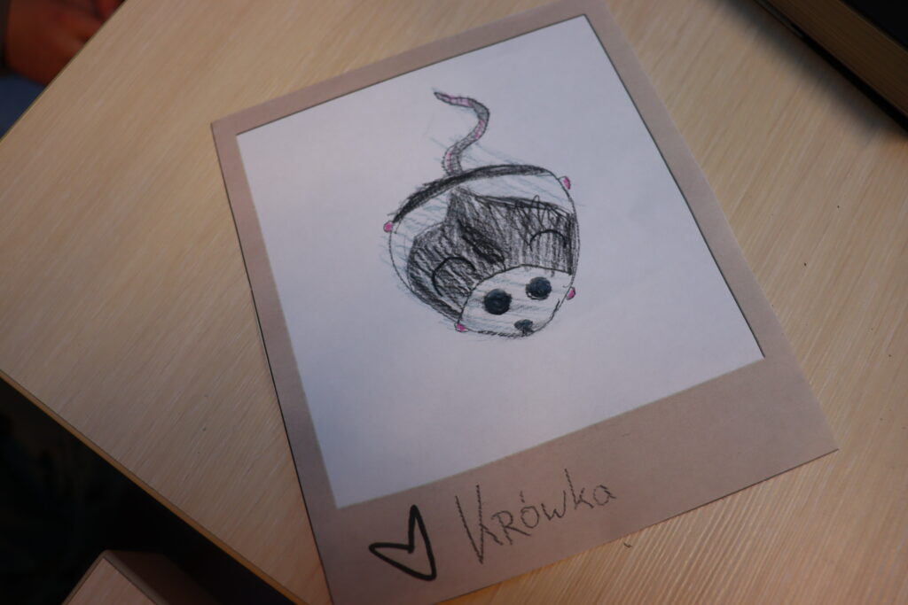 Rysunek przedstawiający małą szarą myszkę podpisaną Krówka.