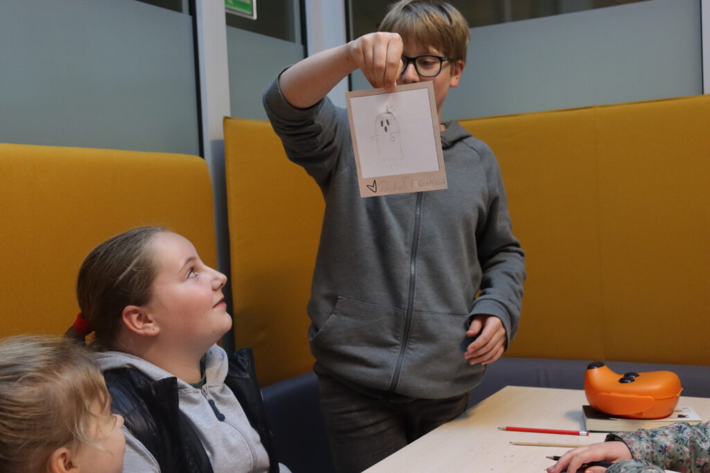 Chłopiec w okularach prezentuje rysunek ducha z podpisem: Duchoł.