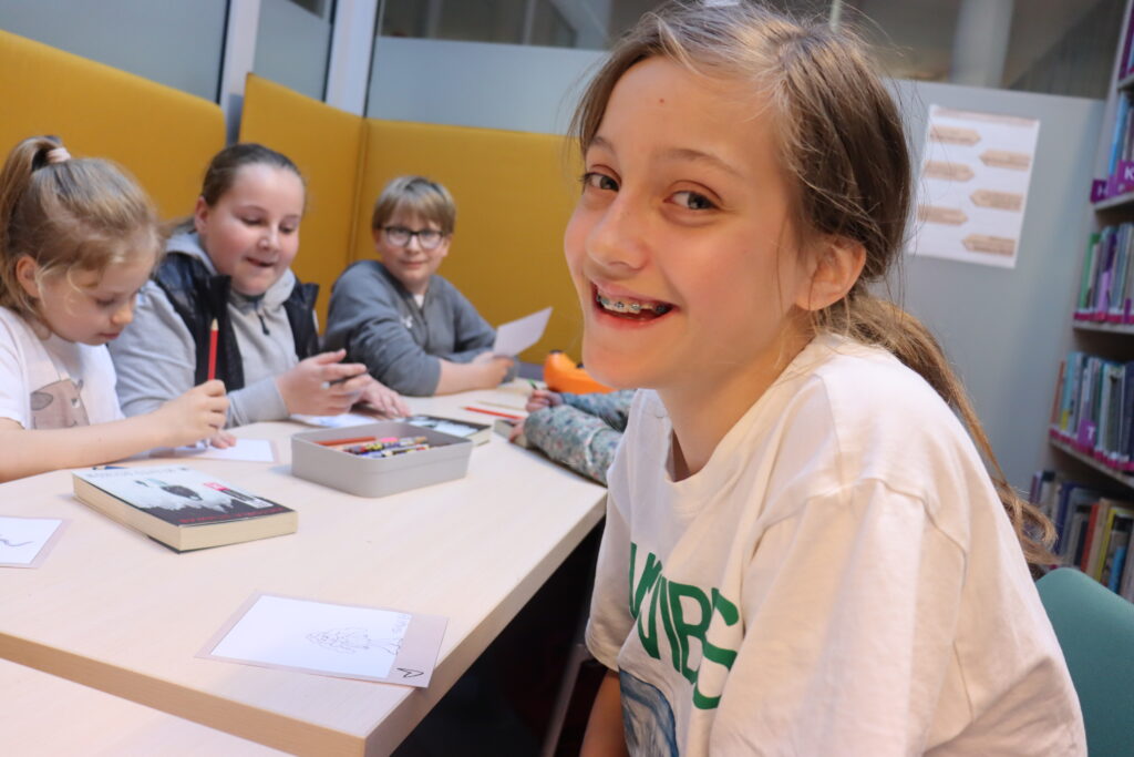 Dziewczynka w jasnej koszulce uśmiecha się do aparatu.