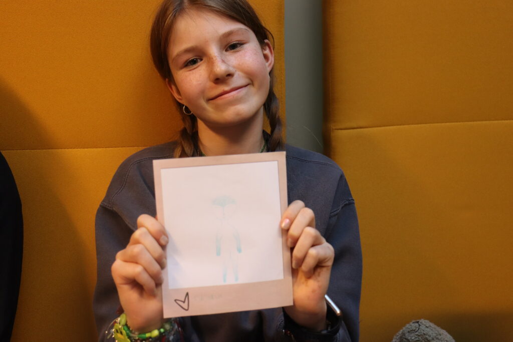Dziewczynka z warkoczami pokazuje swój rysunek ducha.