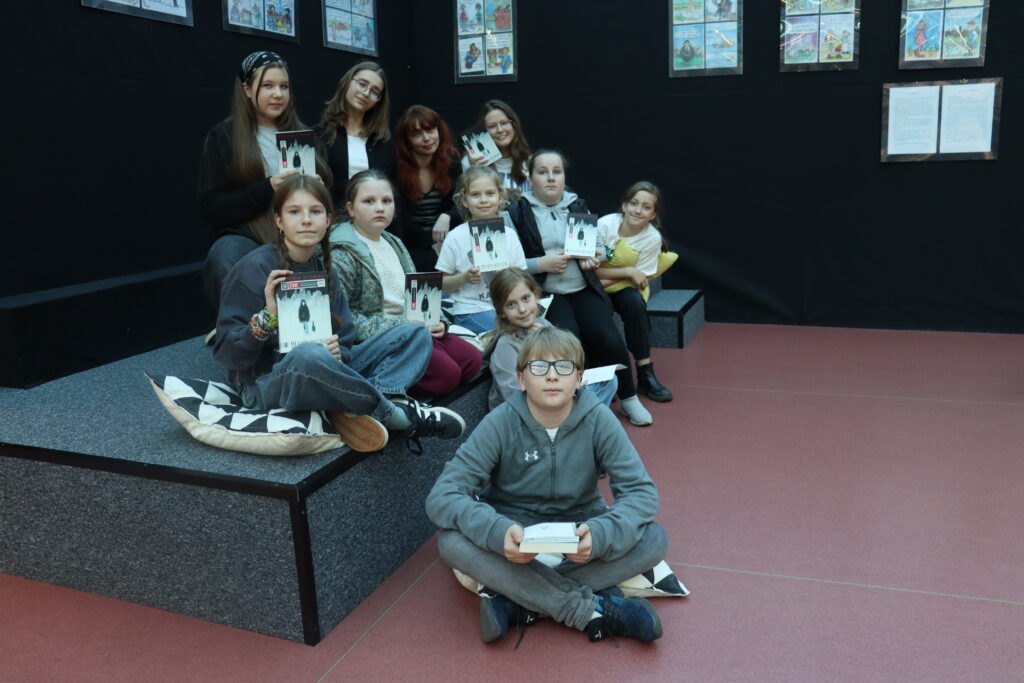 Członkowie klubu pozują na scenie w bibliotece z książkami w dłoniach.