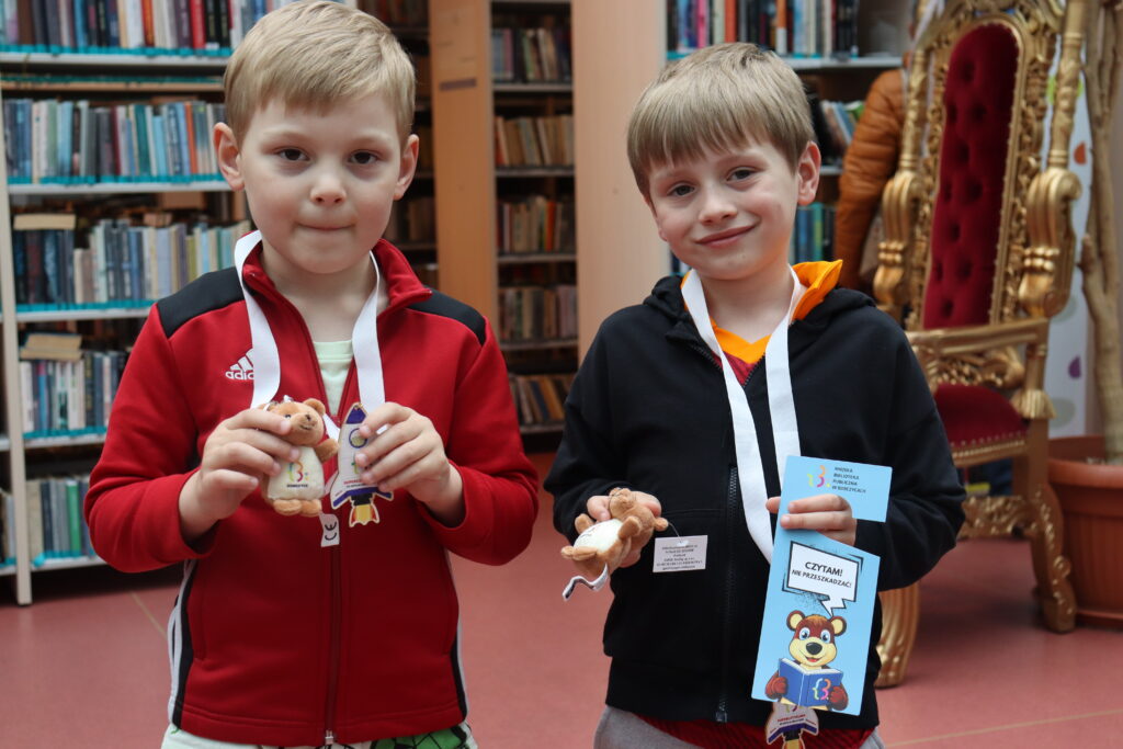 Dwóch małych chłopców z nagrodamiL medalami, pluszowymi misiami i zawieszkami na drzwi.