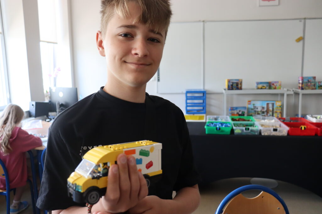Chłopiec w czarnej koszulce trzyma żółtą ciężarówkę LEGO.
