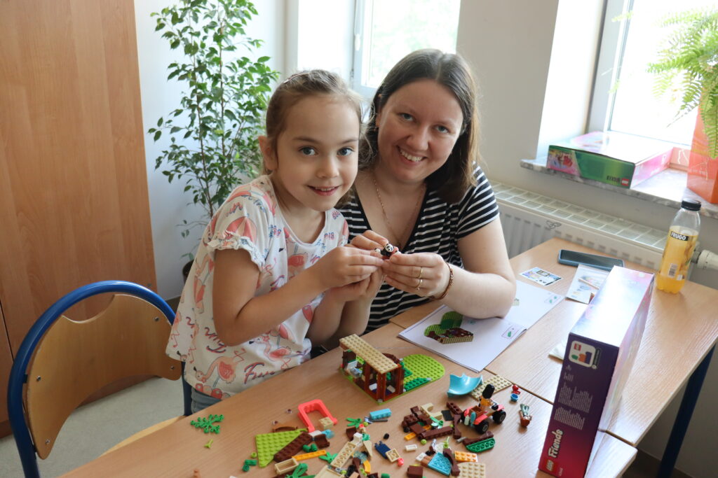Dziewczynka z mamą uśmiechnięte pozują do zdjęcia z klockami.