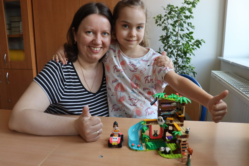 Mama i córeczka pokazują zbudowany domek z LEGO.